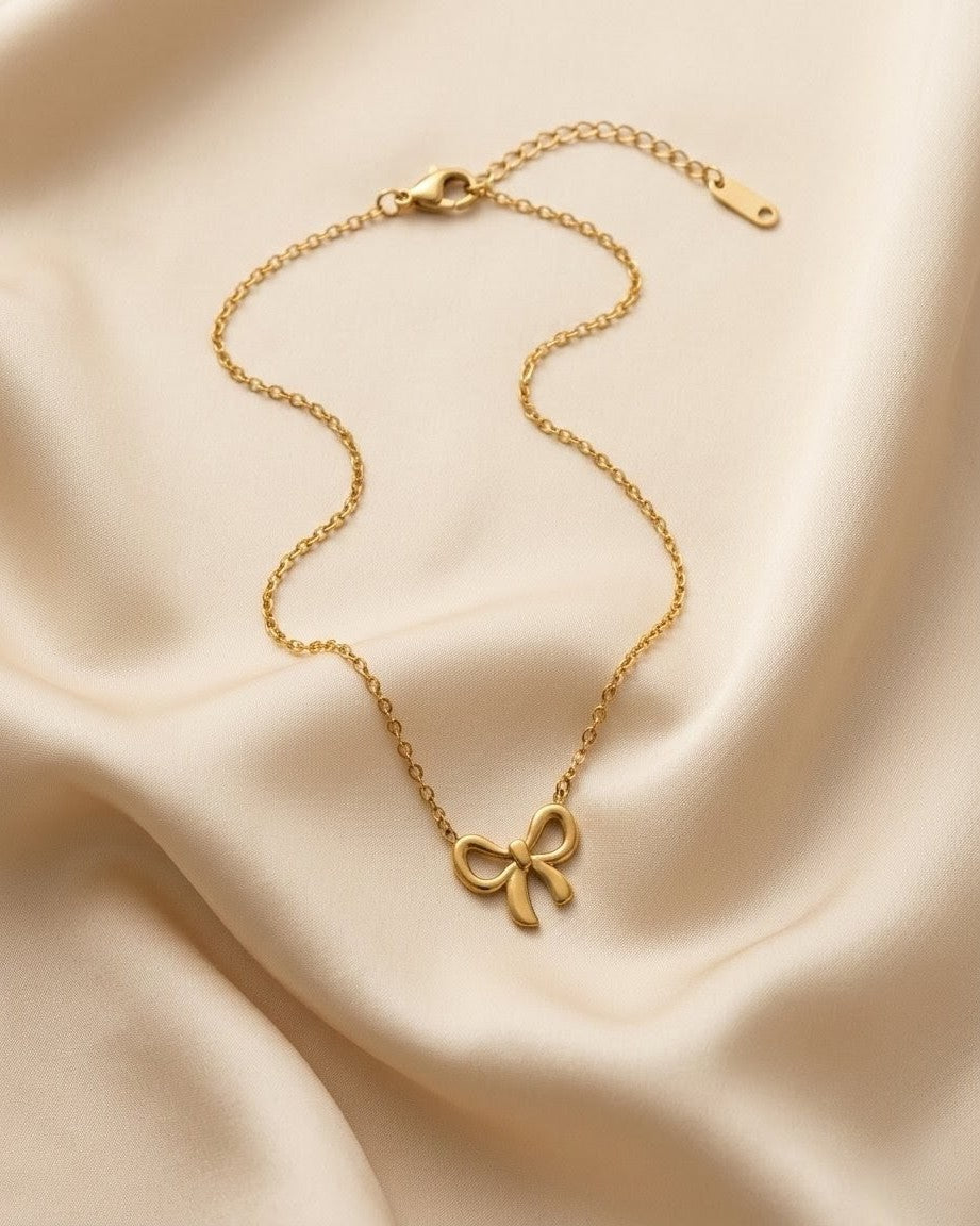 Gold necklace with a bow pendant on a beige fabric background