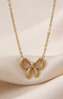 Gold bow-shaped necklace on a soft beige background