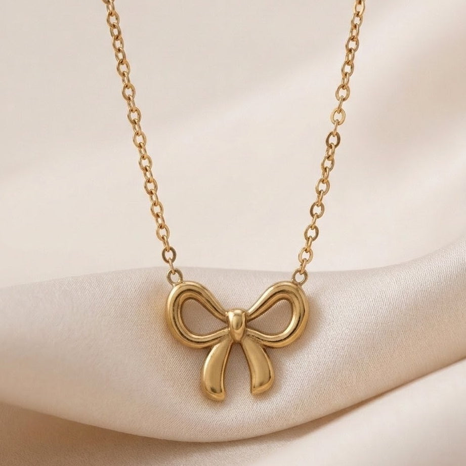 Gold bow-shaped necklace on a soft beige background