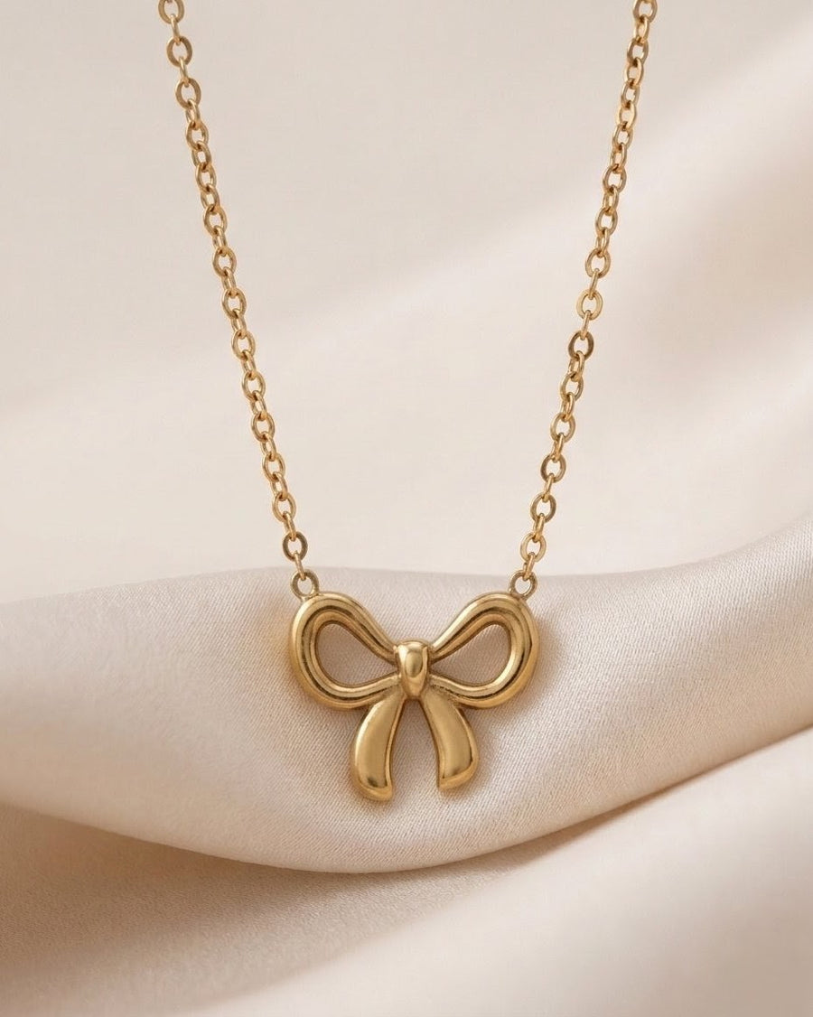 Gold bow-shaped necklace on a soft beige background