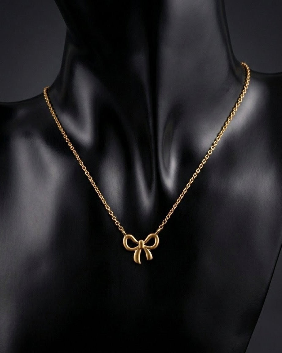 Gold necklace with a bow pendant on a black mannequin