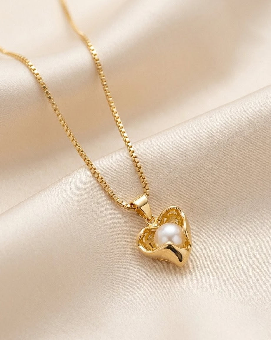 Gold necklace with a heart-shaped pendant featuring a pearl on a beige fabric background