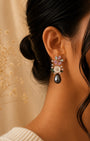 A close-up of a woman's ear wearing a delicate silver 925 floral dangle earring with a large teardrop pearl drop and small pastel gemstone flowers, set against a warm beige background with dried floral decor.