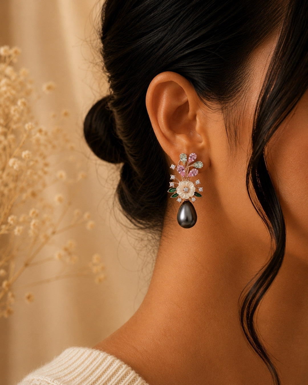 A close-up of a woman's ear wearing a delicate silver 925 floral dangle earring with a large teardrop pearl drop and small pastel gemstone flowers, set against a warm beige background with dried floral decor.