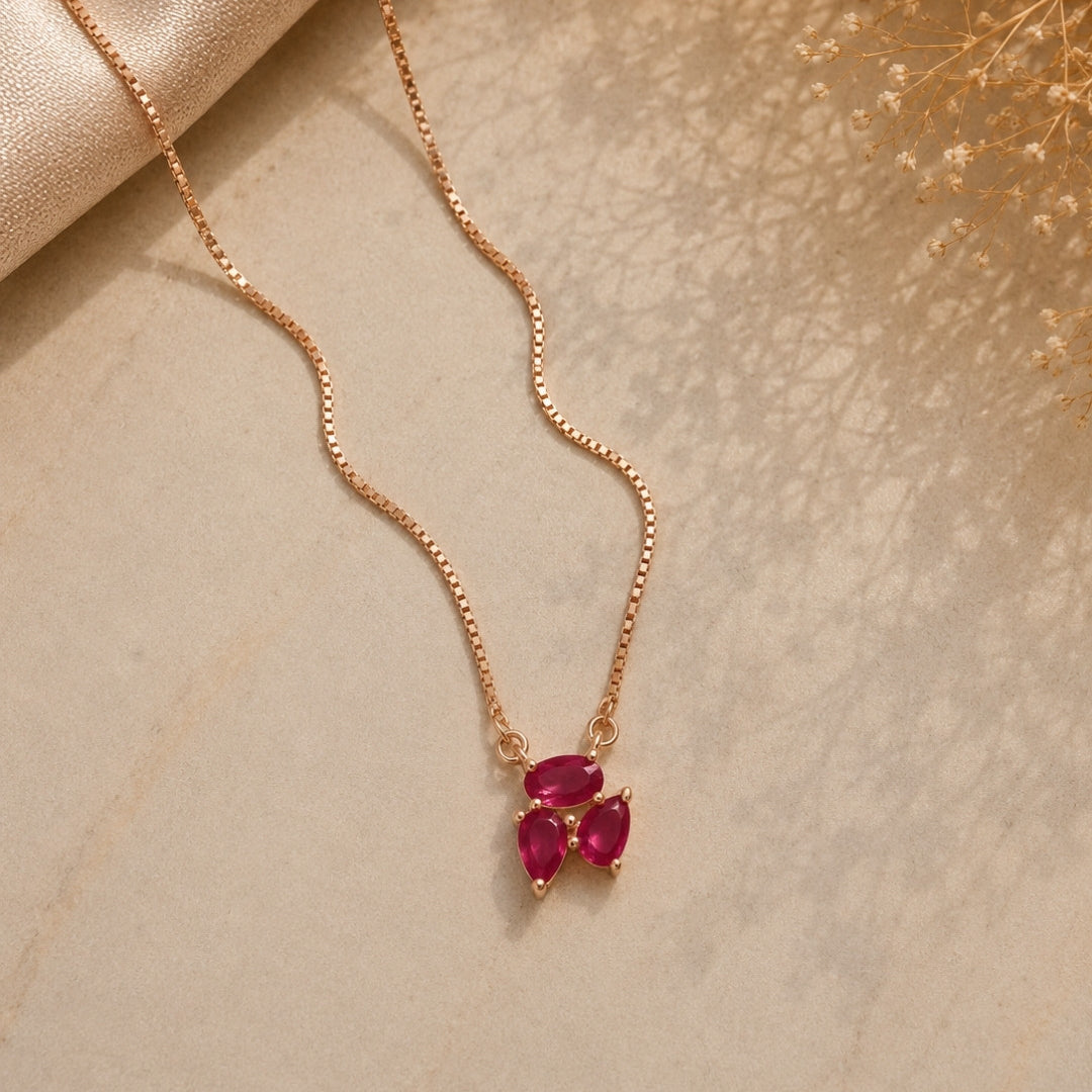 Rose gold necklace with red gemstones on a beige surface