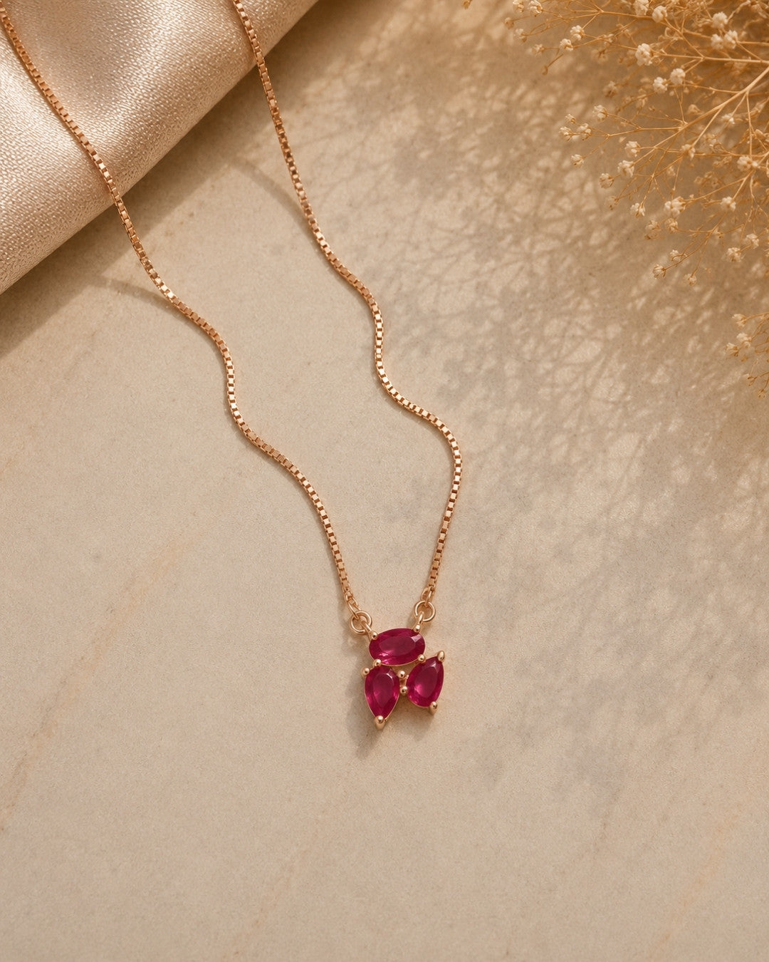 Rose gold necklace with red gemstones on a beige surface