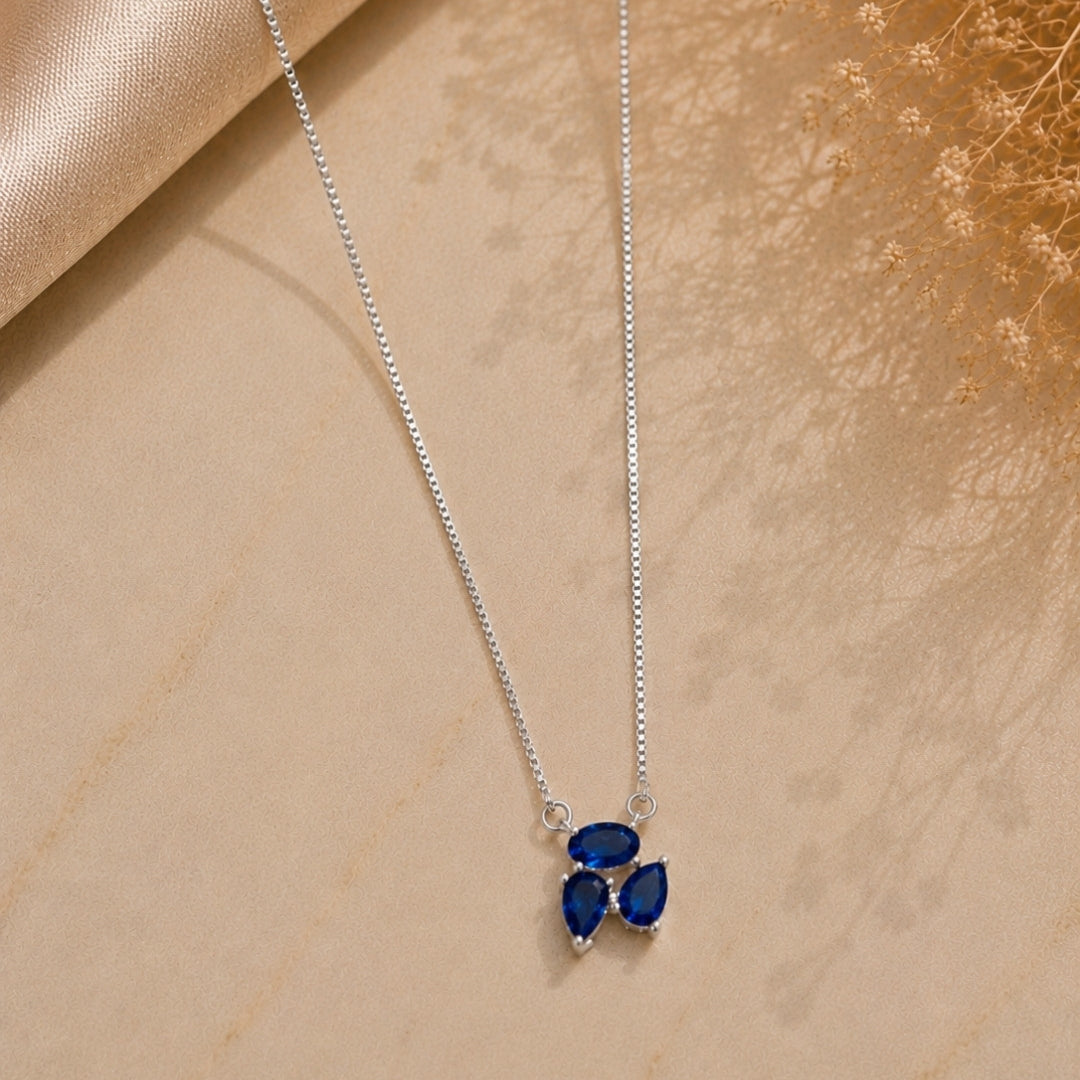 Silver necklace with a blue pendant on a beige surface
