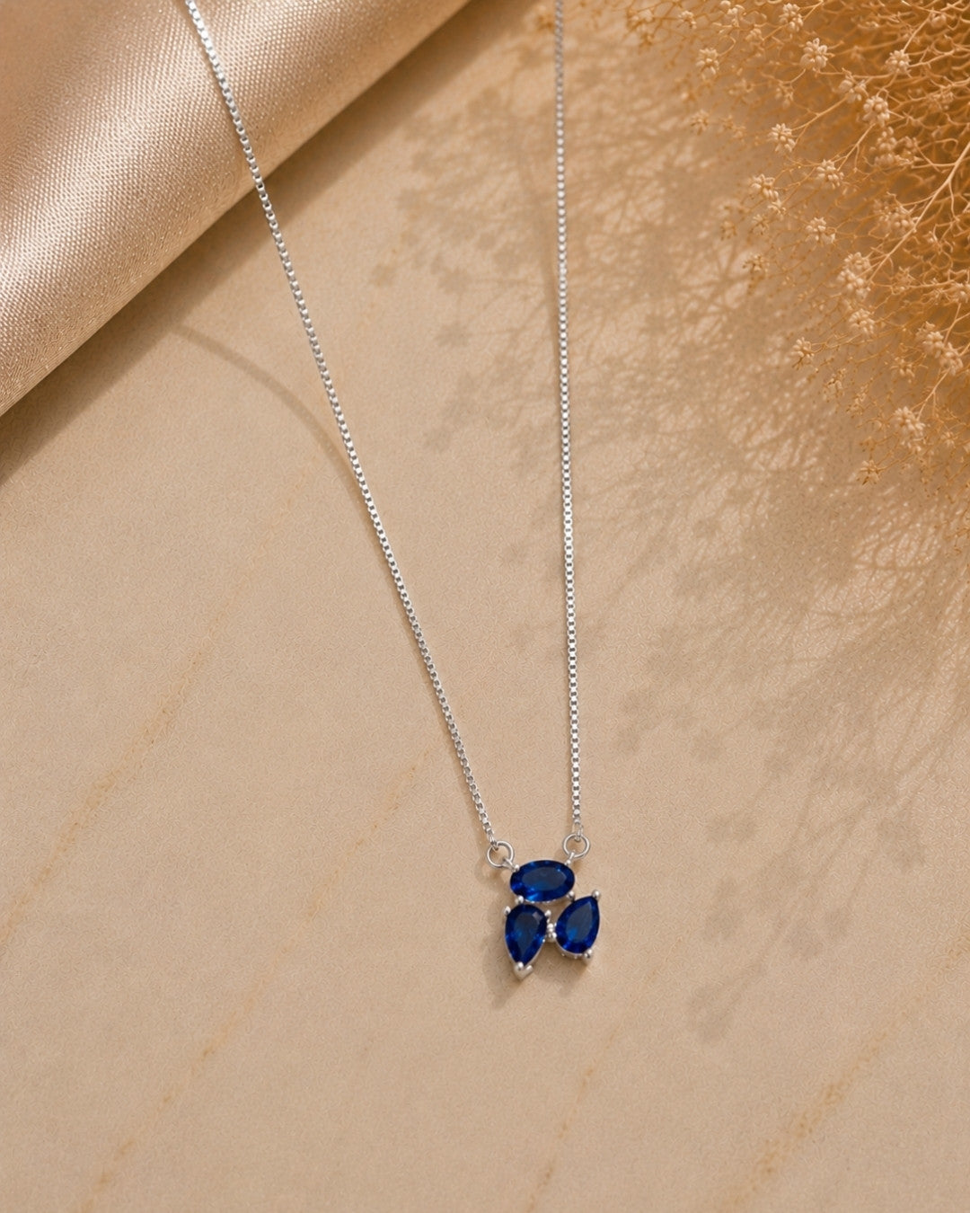 Silver necklace with a blue pendant on a beige surface